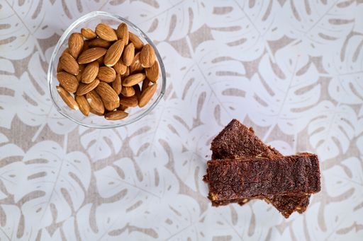 A top view of a stuck of brownies with almonds and nuts and a bowl of almonds on the table