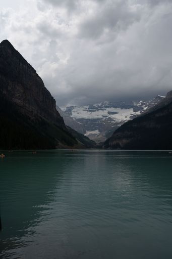 A vertical shot of the turquoise Lake Louise surrounded by high mountains in clouds, Canada