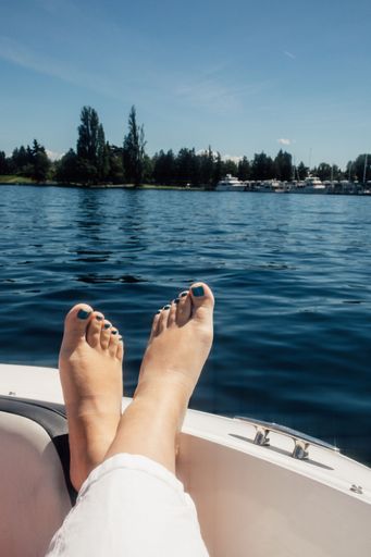 woman in white pants with feet up, relaxing on bow of motor boat during sunny summer day