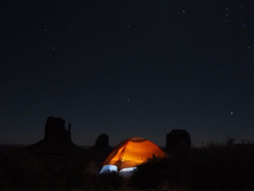night view of a camping tent in the monument valley national park under the stars, with mountain silhouettes in the background