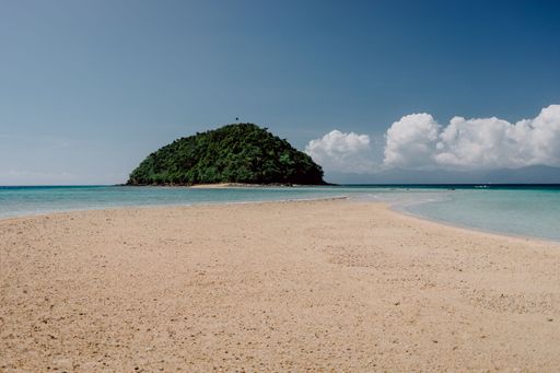 A mesmerizing view of the sandy Bon Bon Beach and a cliff with dense trees in the distance in Romblon, Philippines