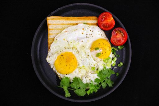 A healthy breakfast with toast bread, fried eggs and cherry tomatoes isolated on black background