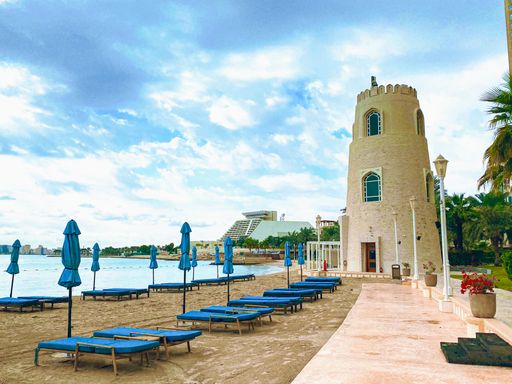 A beautiful shot of blue chairs, umbrellas, and a stone tower on the beach in Qatar