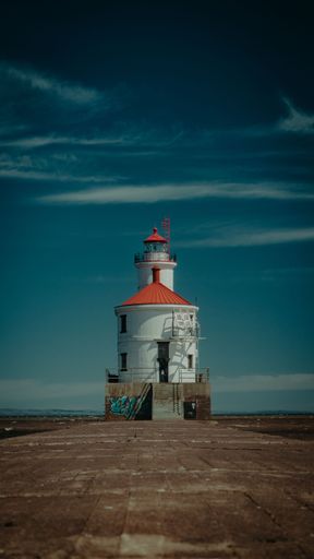 A vertical shot of a lighthouse in the background of a cloudy sky.