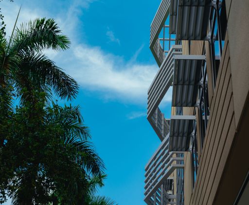 A low angle shot of a modern building exterior with balconies near palm trees