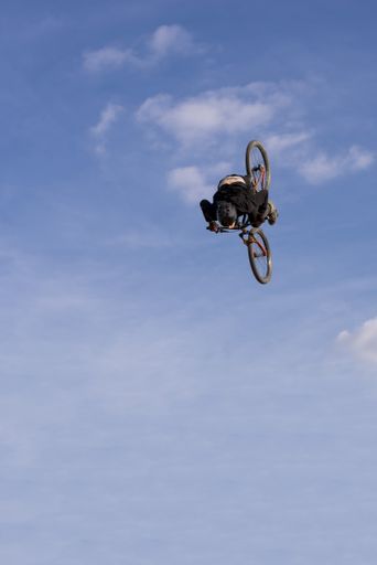 A vertical shot of a biker flying on blue sky and white clouds background