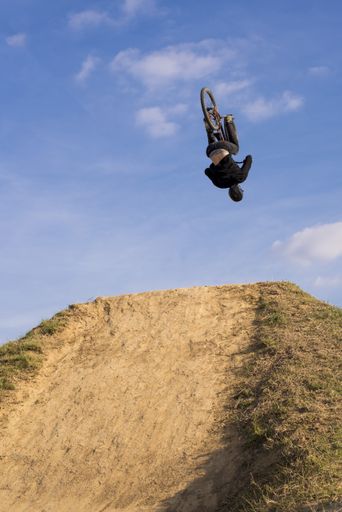 A vertical shot of a mountain biker jumping and flying over a hill