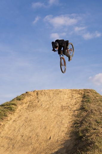 A vertical shot of a biker jumping over a ramp on blue sky background