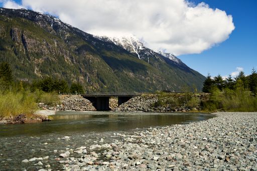 View of a bridge on a remote road and the snow capped mountains behind it from a shallow riverbed.