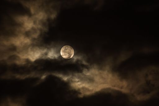 A beautiful view of a full moon lighting between the dark night clouds