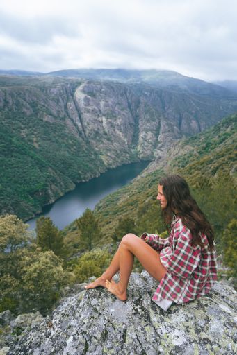 A vertical shot of a young Caucasian woman sitting on the stone in Sil Canyon in Spain