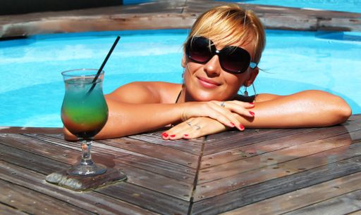 A closeup shot of a smiling blonde female with a juice cup in the pool