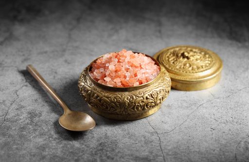 A bowl of Himalayan pink salt in a golden bowl with a golden lid and spoon on the kitchen table