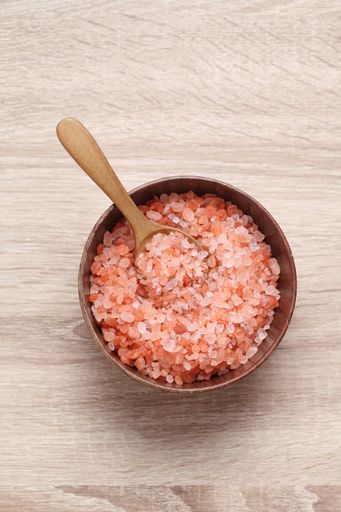A bowl of Himalayan pink salt in a wooden bowl with a wooden spoon on the kitchen table
