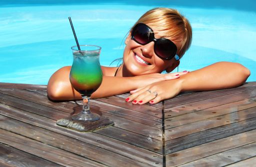 A closeup shot of a smiling blonde female with a juice cup in the pool