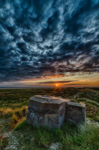 A beautiful scenery of a rock formation in a green field under the breathtaking clouds during sunset