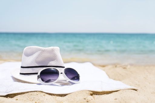 A selective focus shot of sunglasses and a white hat on sandy beach