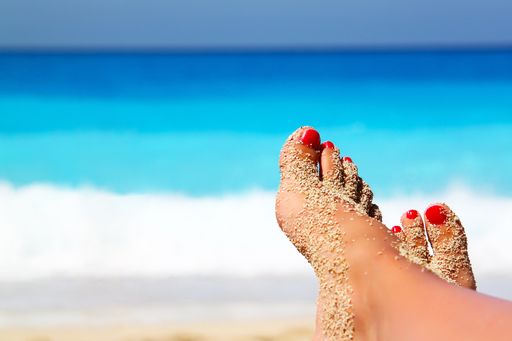 A shallow focus shot of sandy female feet with a red pedicure in the beach
