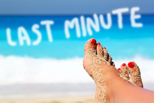 A selective focus shot of female feet on a sandy beach with LAST MINUTE text on the background