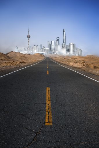 A vertical shot of a sunny asphalt road with desert sand on the sides and a blue sky on the horizon in Shanghai, China
