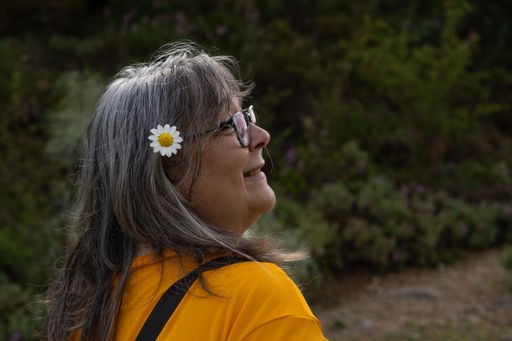 white-haired woman with glasses and orange T-shirt in the forest with a daisy in her hair