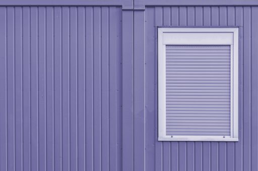 A beautiful shot of a purple metal garage wall with a white window with blinds