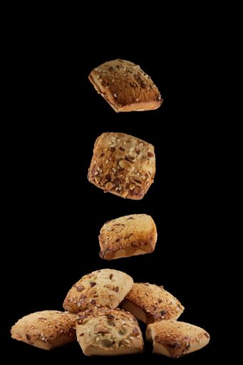 A vertical shot of freshly baked chocolate chips cookies falling on the black surface isolated on black background