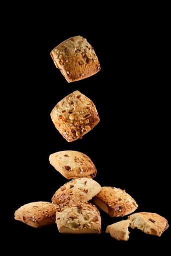 A vertical shot of freshly baked chocolate chips cookies falling on the black surface isolated on black background