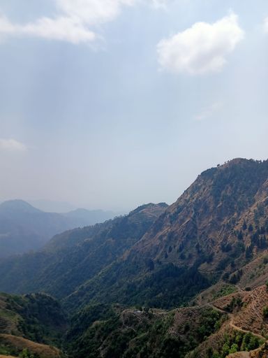 A vertical shot of the mountain range covered with green vegetation against the sky.
