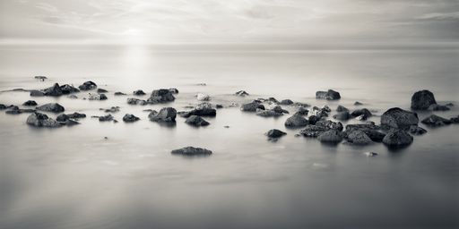 A beautiful shot of some rocks at a beach near a sea in grayscale