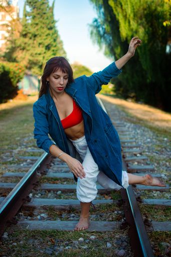 A vertical shot of a Hispanic female dancing barefoot on a train track