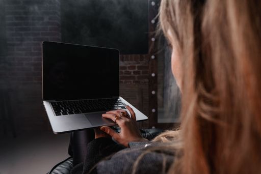 A selective focus shot of a Caucasian brown-haired girl holding her grey laptop in a studio