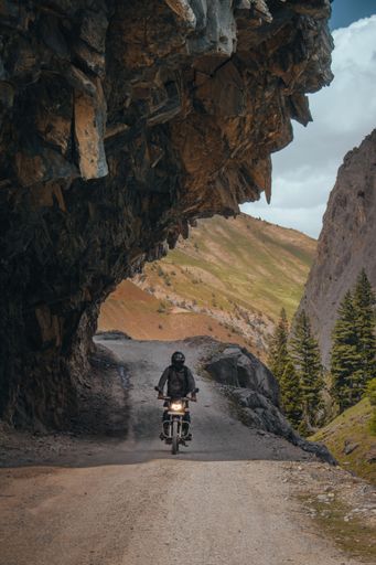 A vertical shot of a motorcyclist with helmet riding a bike on a road under a cliff