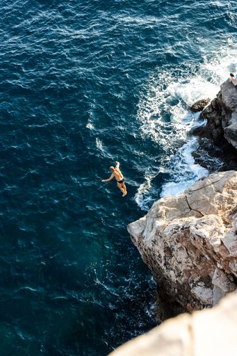 A vertical shot of a man jumping from a cliff into the Adriatic Sea in Dubrovnik, Croatia
