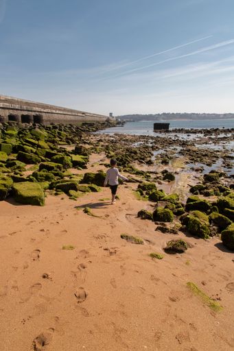 A vertical shot of a female walking on Socoa Port in France with a pretty skyscape in the background