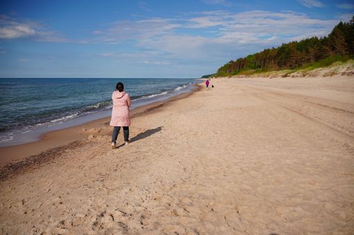 A middle aged chubby female in a pink rainjacket walking barefoot on the beach