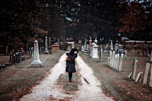 A back view of a female dressed as a witch walking in a cemetery