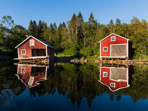 A beautiful view of barns by a reflective lake with trees