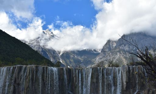A beautiful view of a big waterfall with mountains under the blue cloudy sky