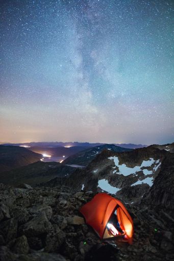 A vertical shot of an orange tent in the rocky mountains under the beautiful starry sky at night