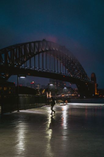 A vertical shot of a person in front of the Sydney Harbor Bridge in Australia during nighttime