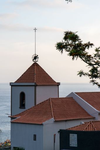 A vertical shot of a bell tower against a blue cloudy sky in Calheta, Madeira