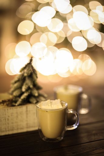 A vertical shot of a cup of hot coffee latte in front of Christmas tree on rustic table