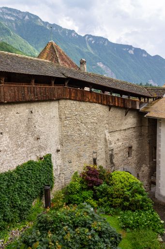 A vertical shot of the medieval Chillon castle in Veytaux, Switzerland, with mountains and a cloudy sky in the background