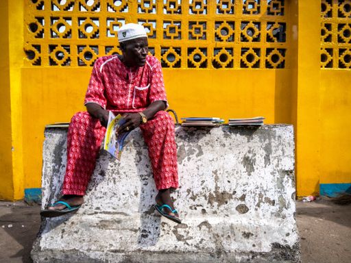 An older African male in a traditional red costume sitting on a slab in Lagos, Nigeria