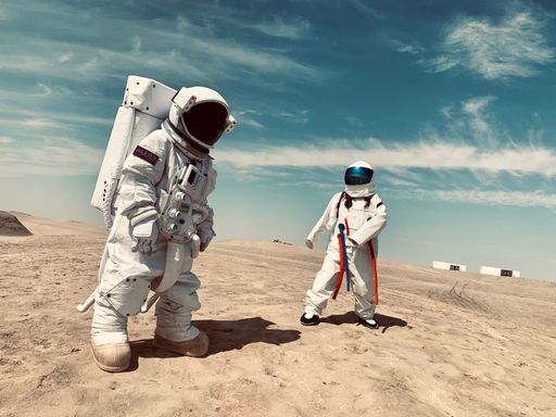 Two astronauts in white spacesuit costumes walking on the sandy surface under the blue clear sky