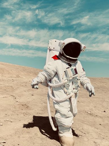 A vertical shot of a person in an astronaut spacesuit walking on the sandy surface under the blue sky