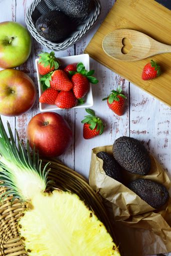 A vertical of varied fresh fruit with strawberries, apples, pineapple and avocados on rustic white wood