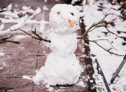 A closeup of a small damaged snowman with tree branches as hands and a carrot as a nose