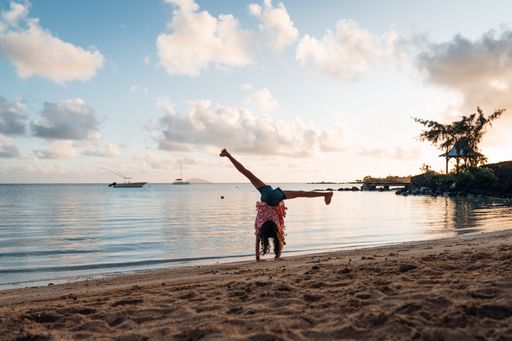 A girl is doing a cartwheel on the beach during the sunrise in Flic en Flac, Mauritius.